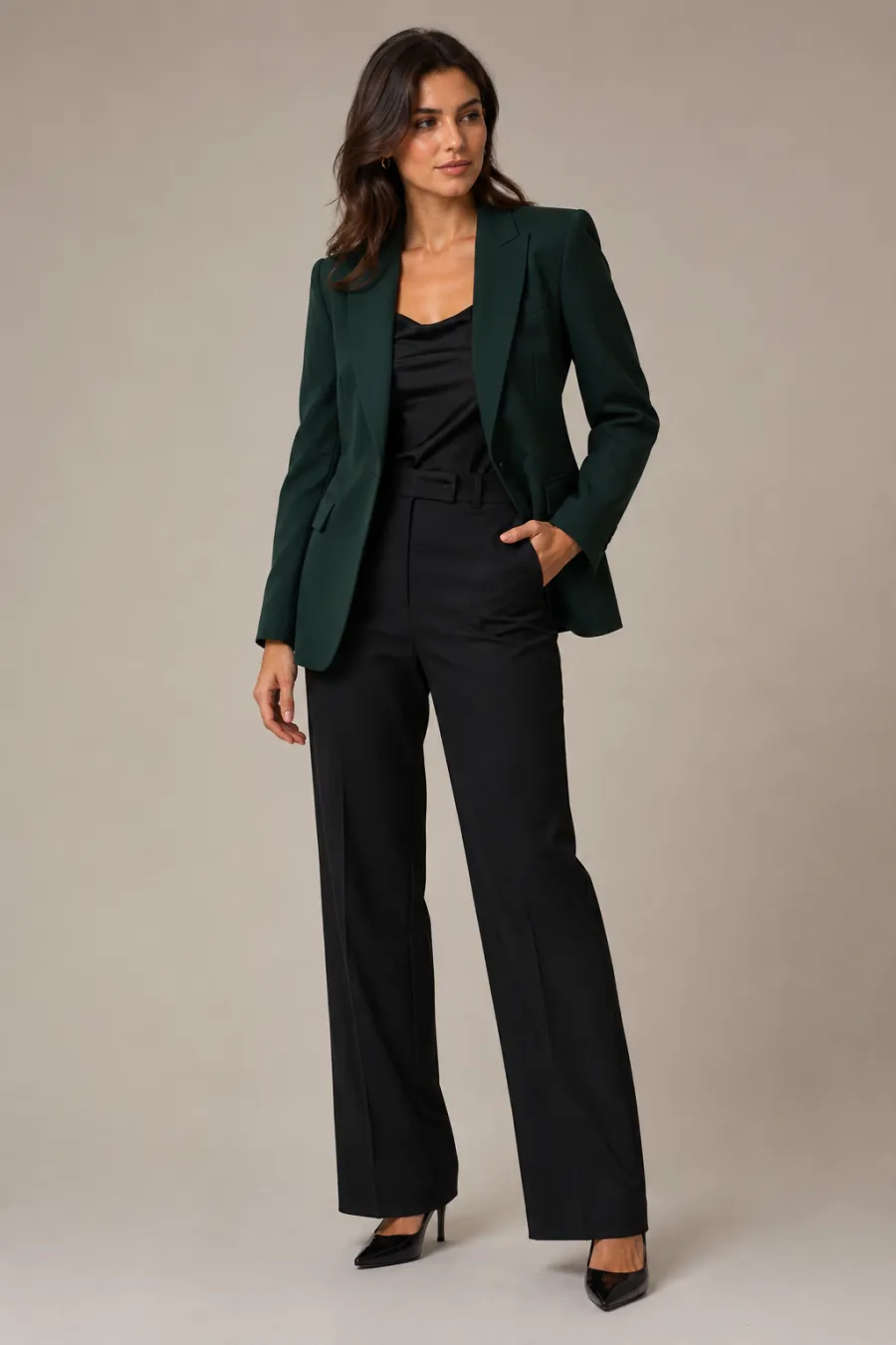 Full-length shot of an office Christmas party look — a structured deep-green blazer over a black top with tailored trousers, on a plain studio background