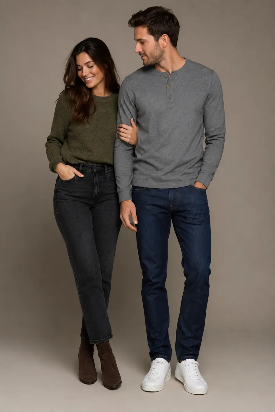 Casual date look: a woman in straight dark jeans, a tucked-in olive-green knit sweater and ankle boots next to a man in indigo jeans, a grey henley and white leather sneakers, plain studio background, full body