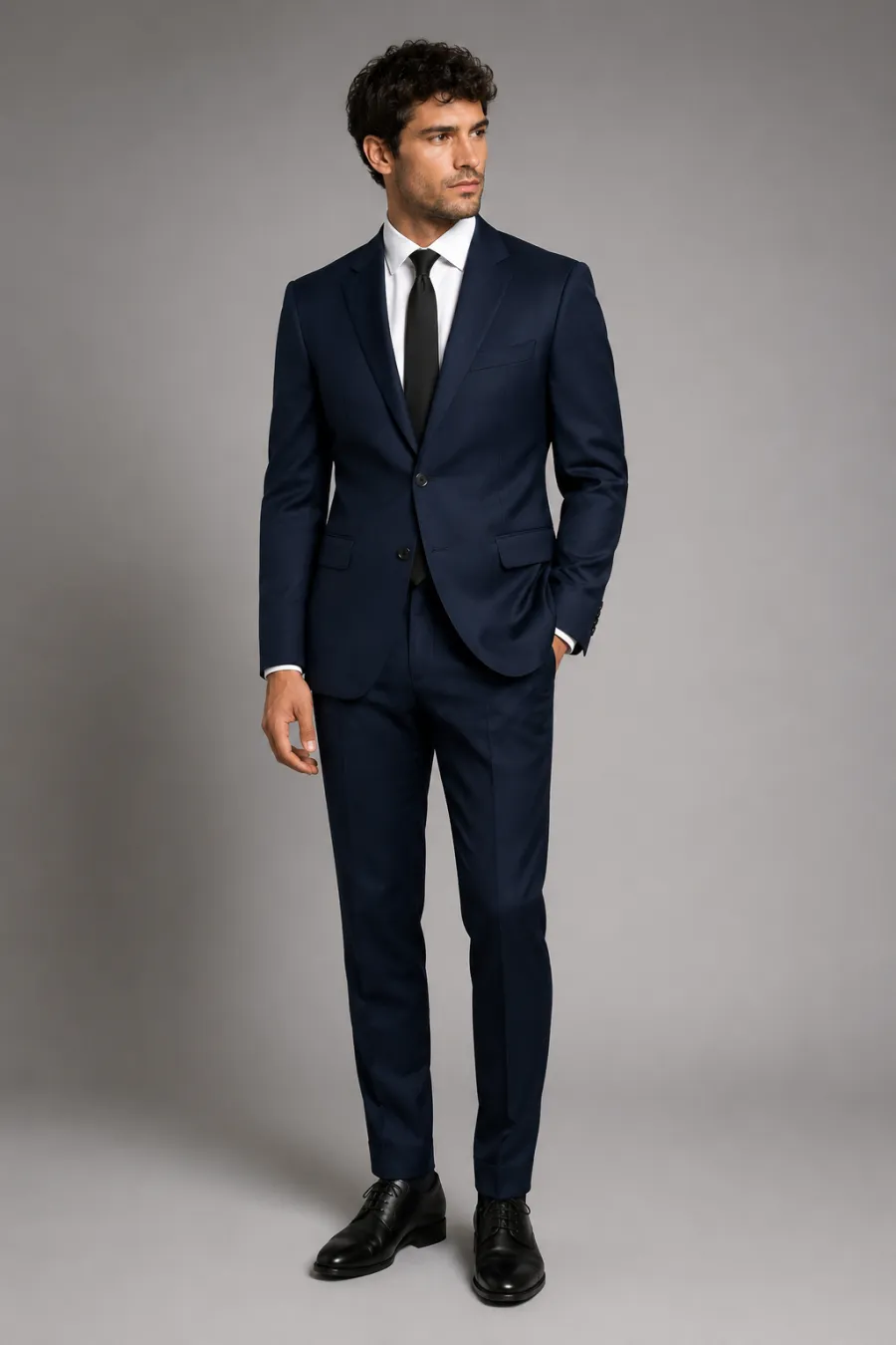 Full body shot of a man in a tailored navy suit, white dress shirt, and plain black tie, polished black shoes, shown on a plain neutral studio background with even lighting