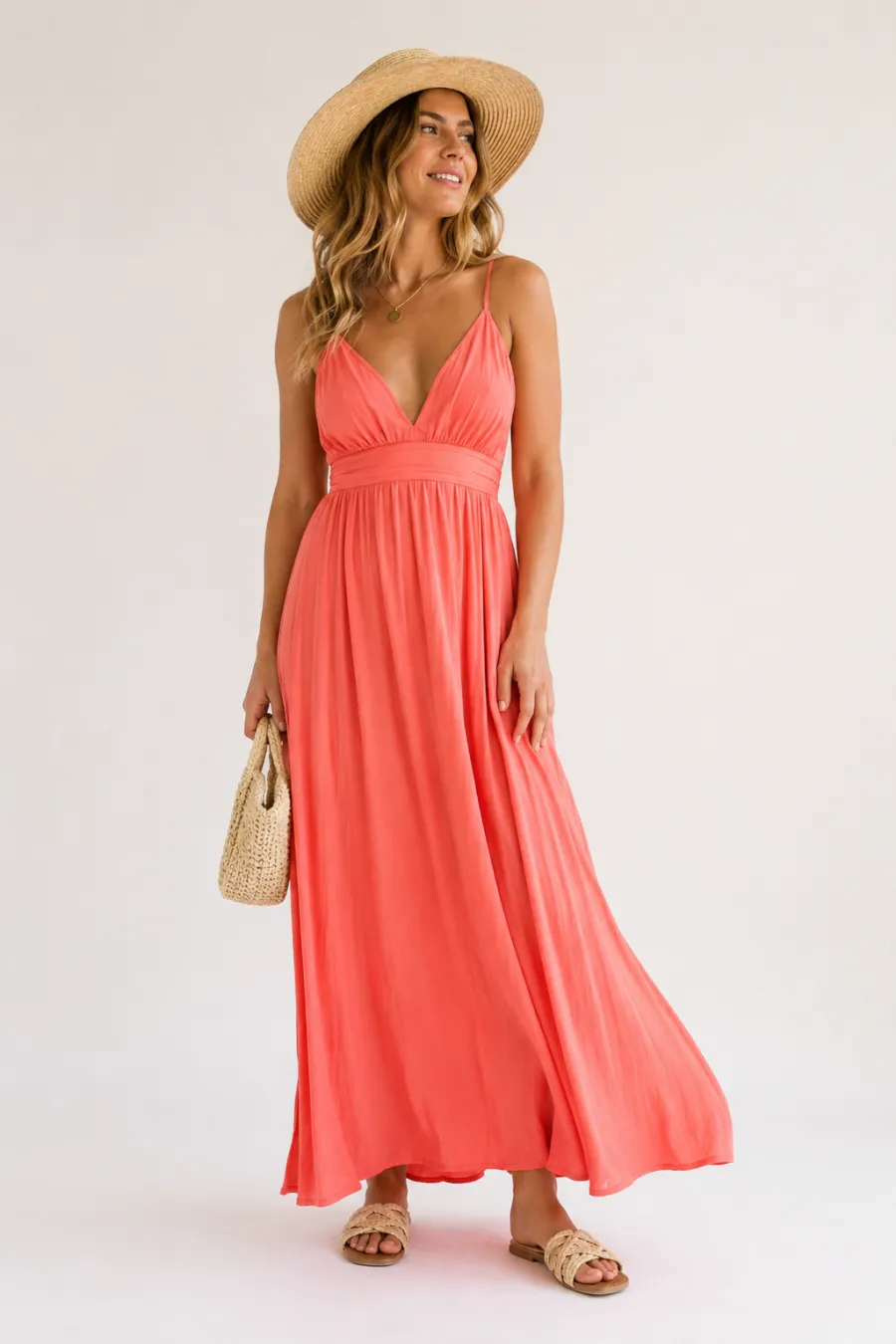A vacation summer outfit on a plain light background — a flowing coral maxi dress with a straw hat and woven sandals, bright airy lighting, full body