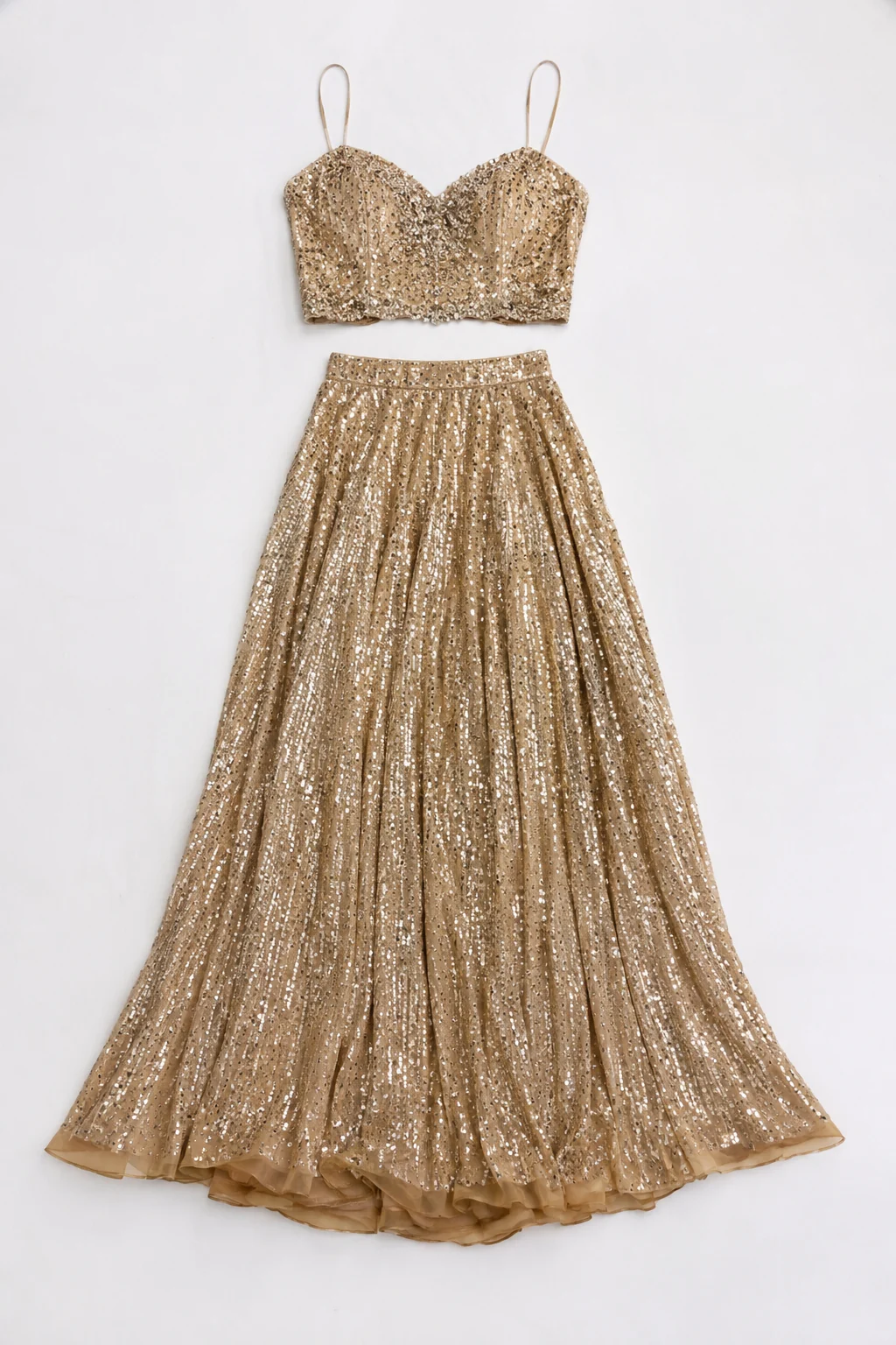 A two-piece gold sequin prom set with a cropped beaded top and long flowing skirt arranged flat on a plain white surface, sparkle visible, no text