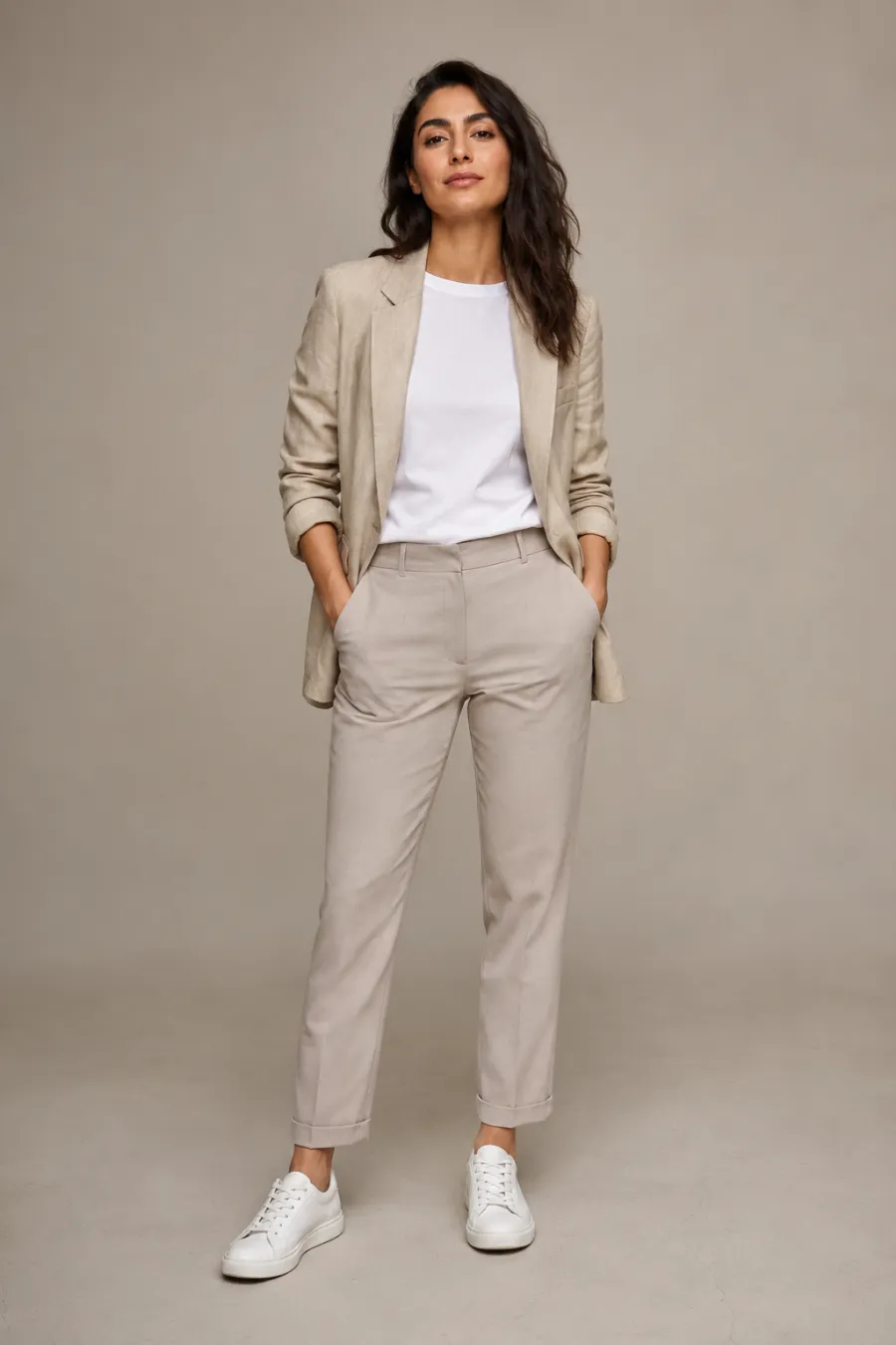 An adult Middle Eastern woman wearing a relaxed beige linen blazer over a plain white crew-neck tee with stone-colored tailored chinos and white minimalist sneakers, confident stance, full body, entire figure from head to feet in frame, centered with headroom