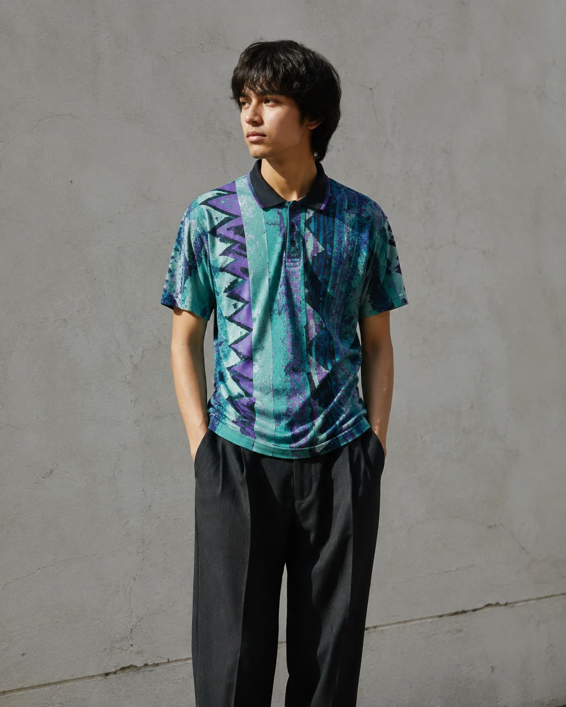 Young adult wearing a vintage 1990s patterned soccer shirt with a collared neck, standing against a neutral wall in daylight, full pattern visible