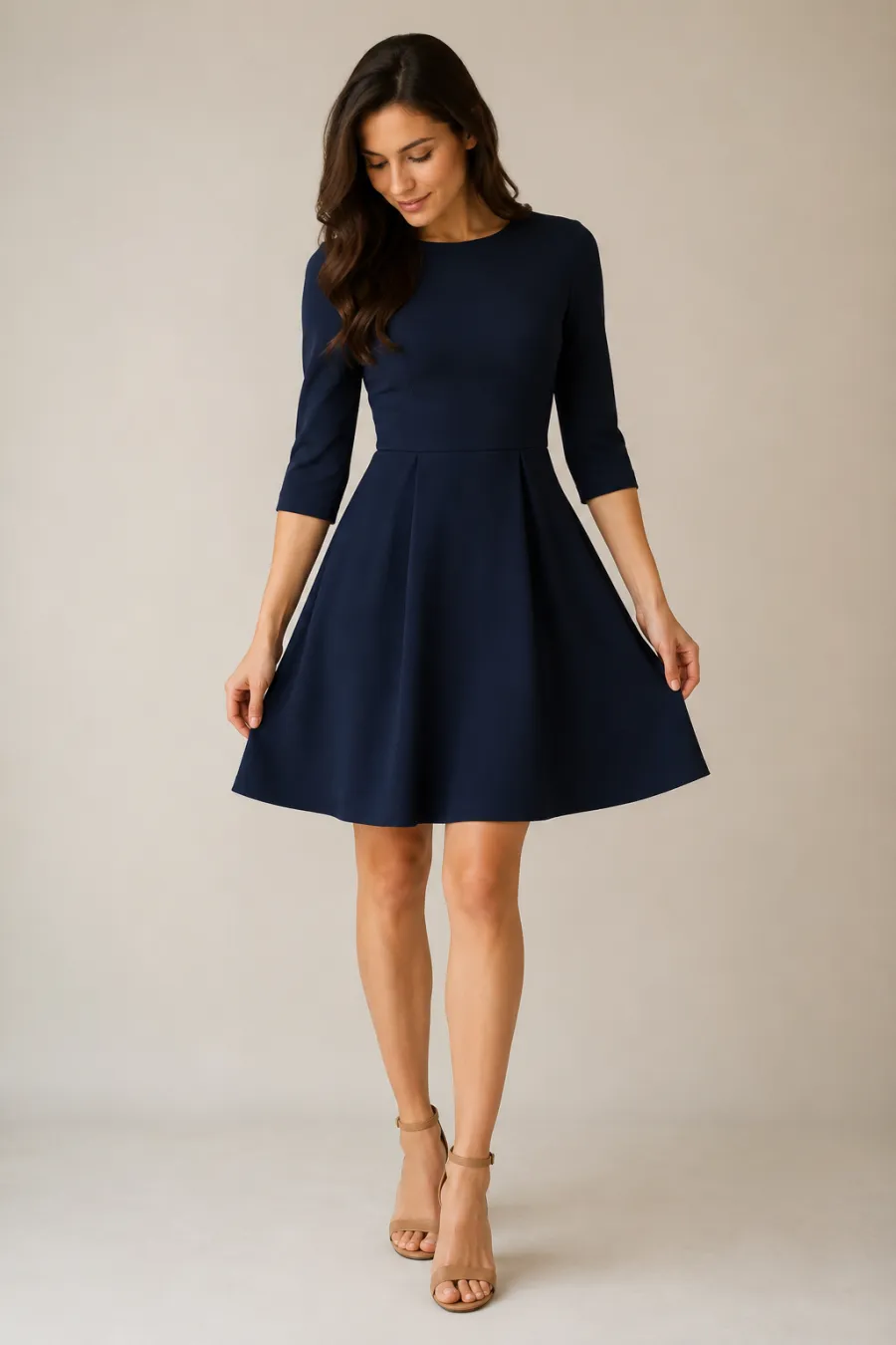 An adult woman trying on a knee-length navy A-line graduation dress with three-quarter sleeves and tan block heels, posing to check the hemline, full body, entire figure from head to feet in frame, centered with headroom