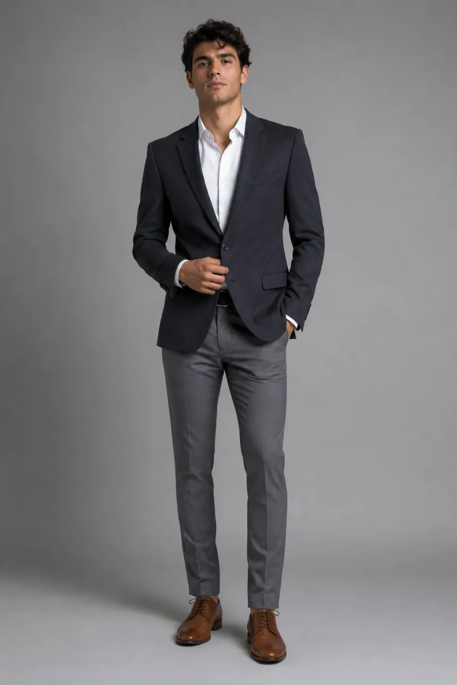 An adult man trying on a charcoal blazer over a white dress shirt with no tie, slim gray trousers, and brown oxford shoes for graduation dinner photos, full body, entire figure from head to feet in frame, centered with headroom